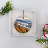 Mountain watercolor holiday ornament presented inside an opened white gift box ready for gifting.