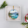 Ceramic travel ornament nestled carefully inside an open white gift box ready for holiday gifting.