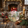 Holiday ornament styled on a rustic tabletop decorated with festive pinecones and a candle.