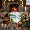 Scenic waterfall ornament resting on a rustic holiday table surrounded by pinecones and gentle candlelight.