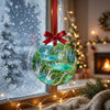 Holiday travel ornament suspended in front of a frosty winter window in soft daylight.