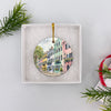 Round ceramic holiday ornament presented inside an open white gift box ready for festive giving.
