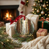 Holiday ornament resting next to wrapped gifts with a cozy glowing fireplace in the background.